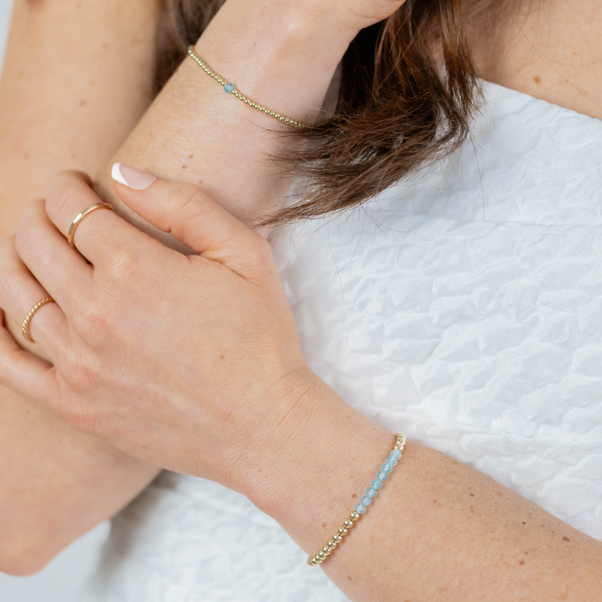 Close-up of hands wearing gold bracelets and rings on a light background