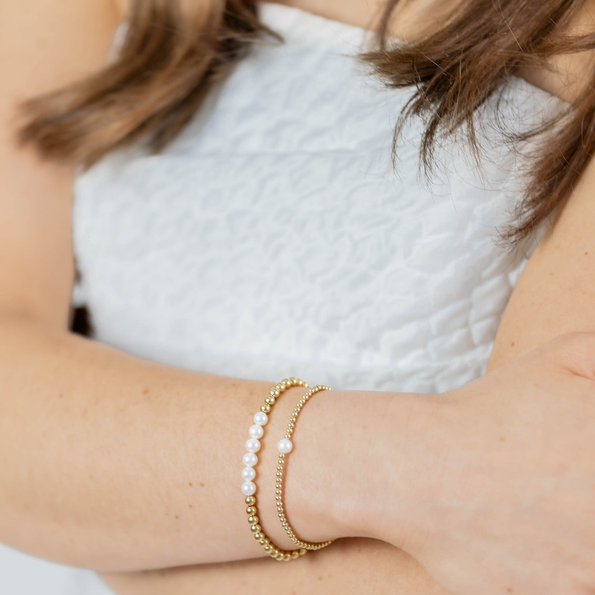 Close-up of a person wearing gold bracelets with pearl accents on a blurred background