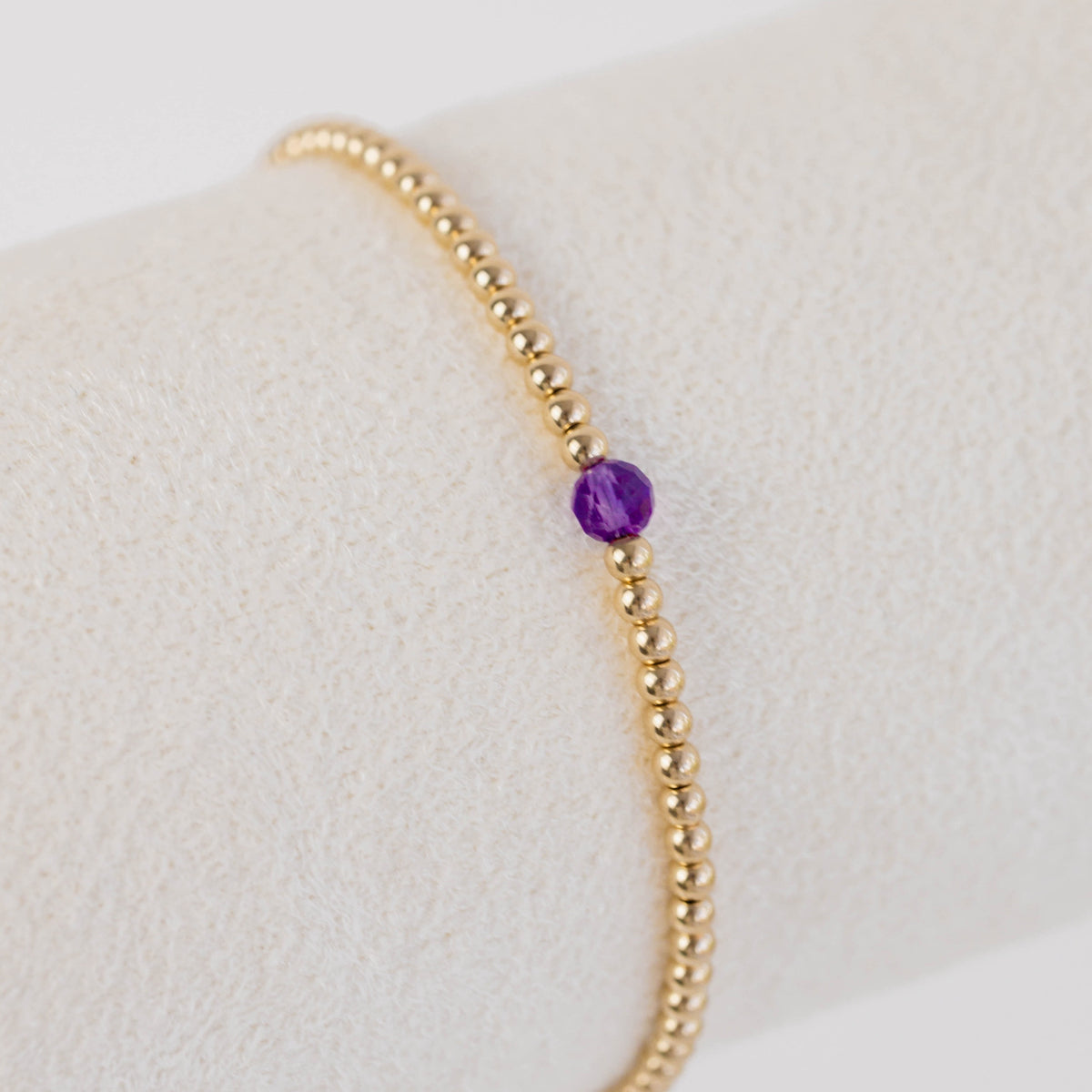 Gold beaded bracelet with a purple gemstone on a light gray background