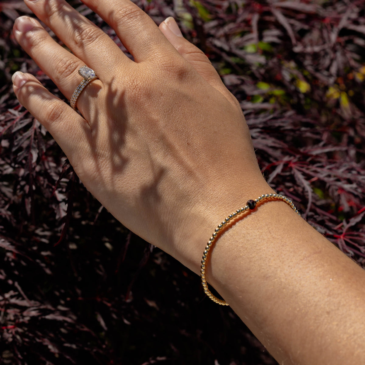 Hand wearing a ring and bracelet against a blurred natural background