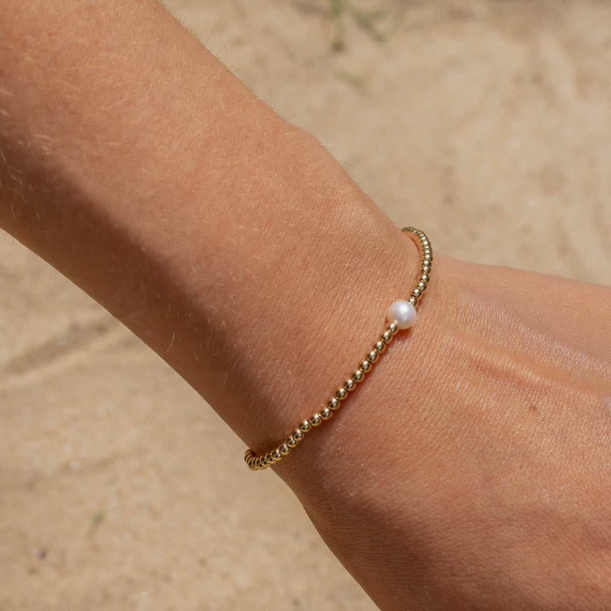 Gold bracelet with a pearl on a wrist against a blurred natural background