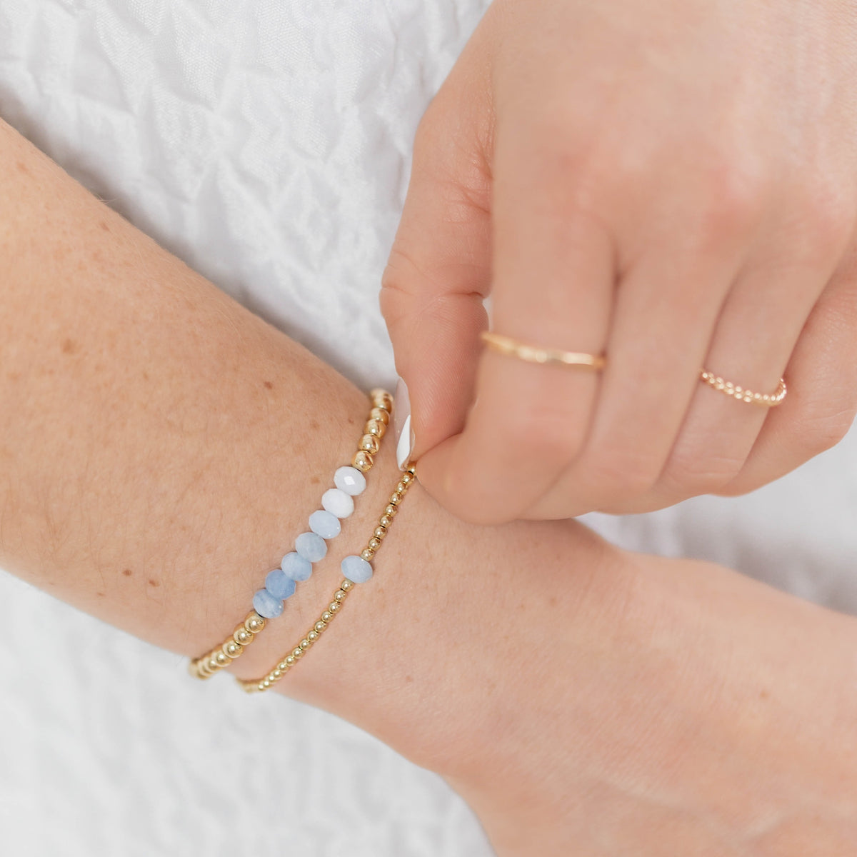 Close-up of a person's wrist wearing gold bracelets with blue beads on a white background