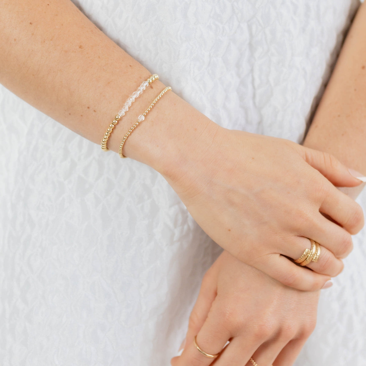 Close-up of a person's wrist with gold bracelets and rings on a white background