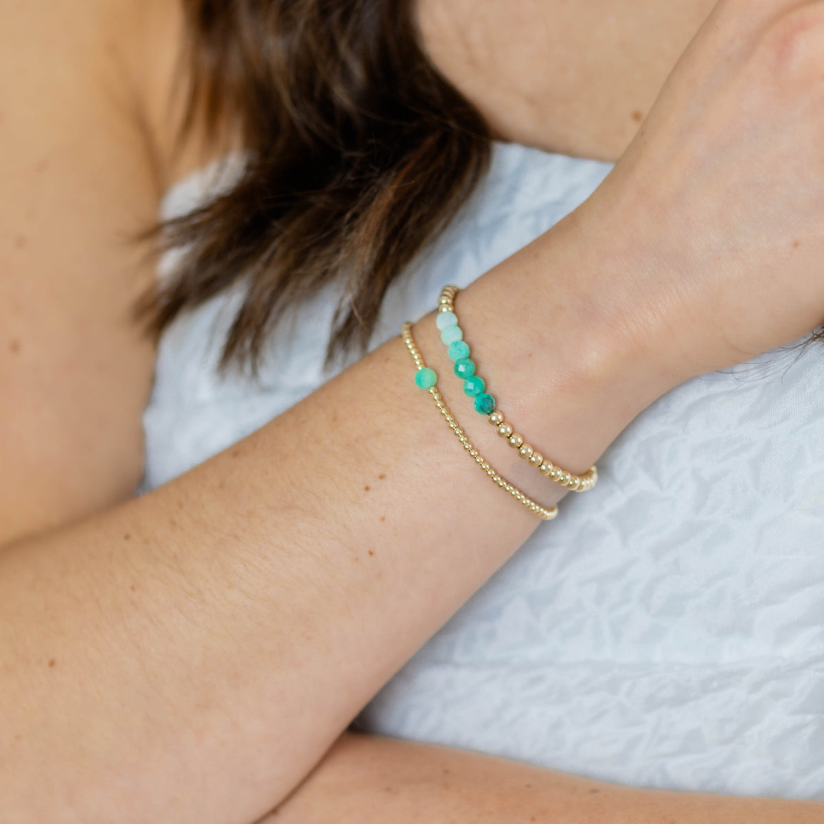 Close-up of a person's wrist wearing two gold bracelets with green beads on a light background.