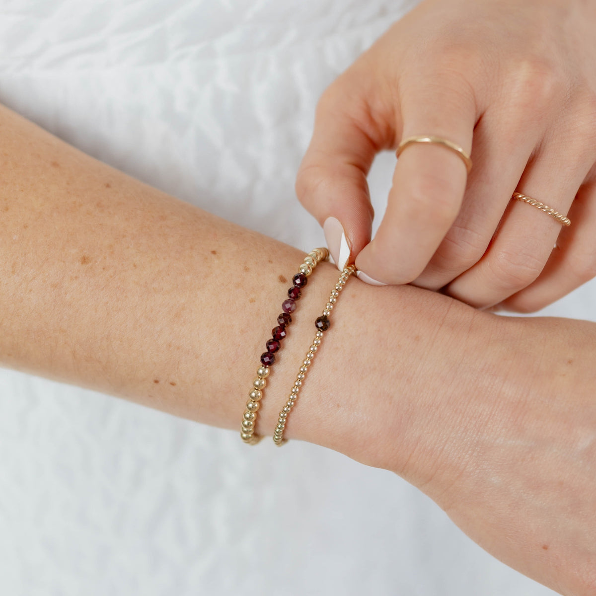 Person wearing a gold bracelet with small beads on a white background