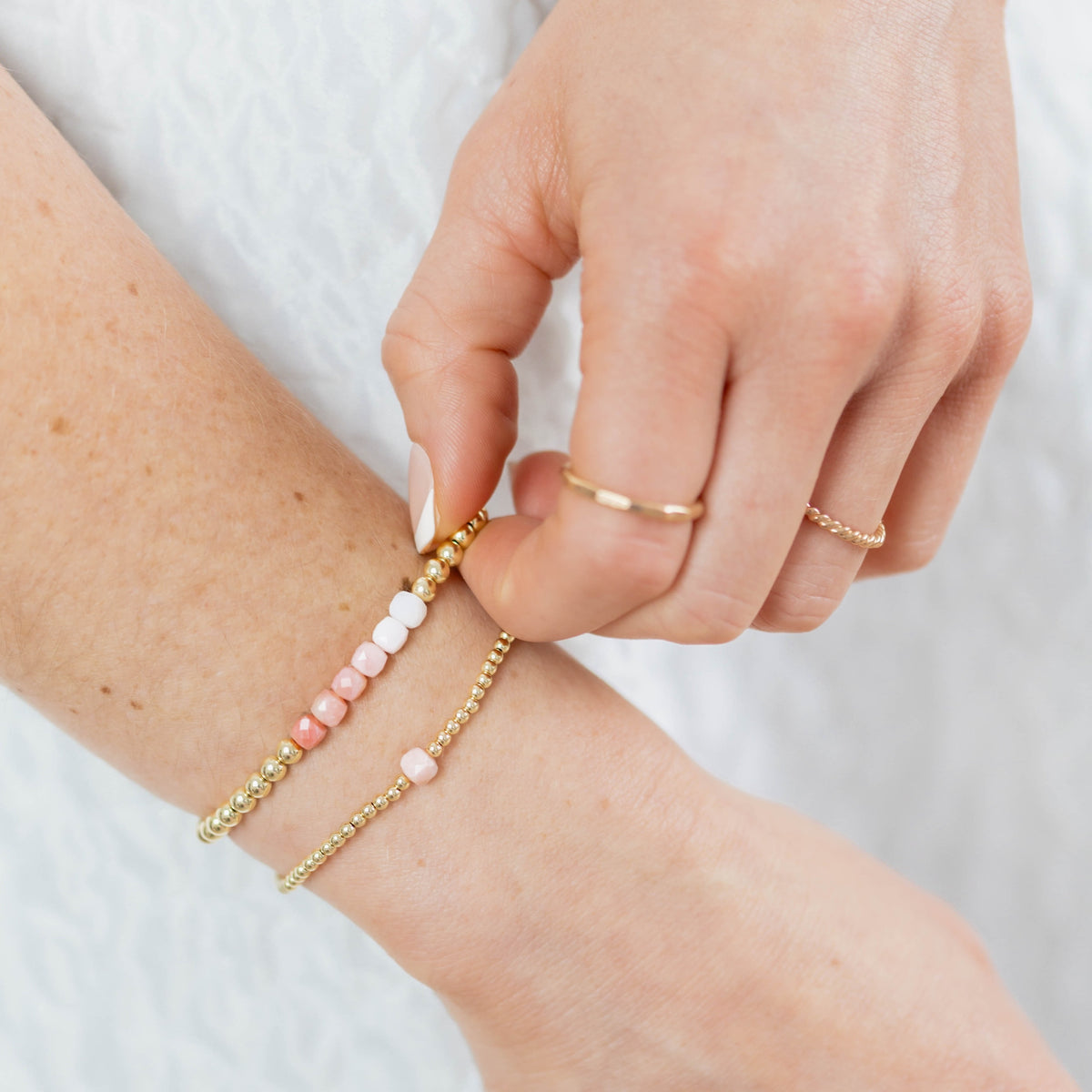 Person wearing a gold bracelet with pink beads on a white background