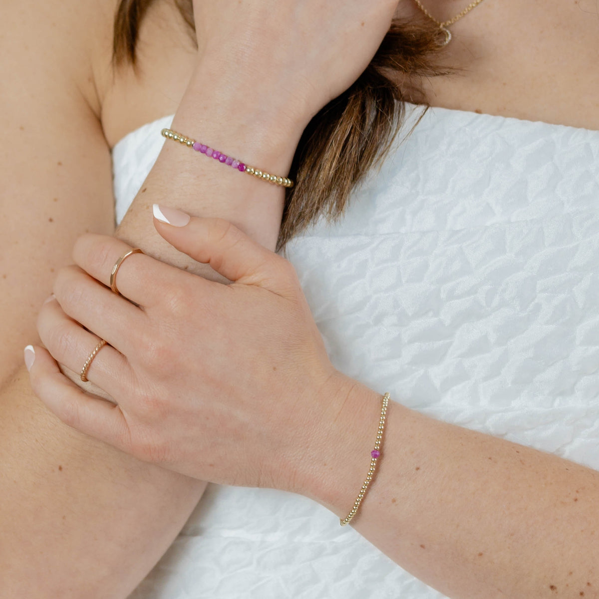 Close-up of a person's arm with gold bracelets and rings on a white background
