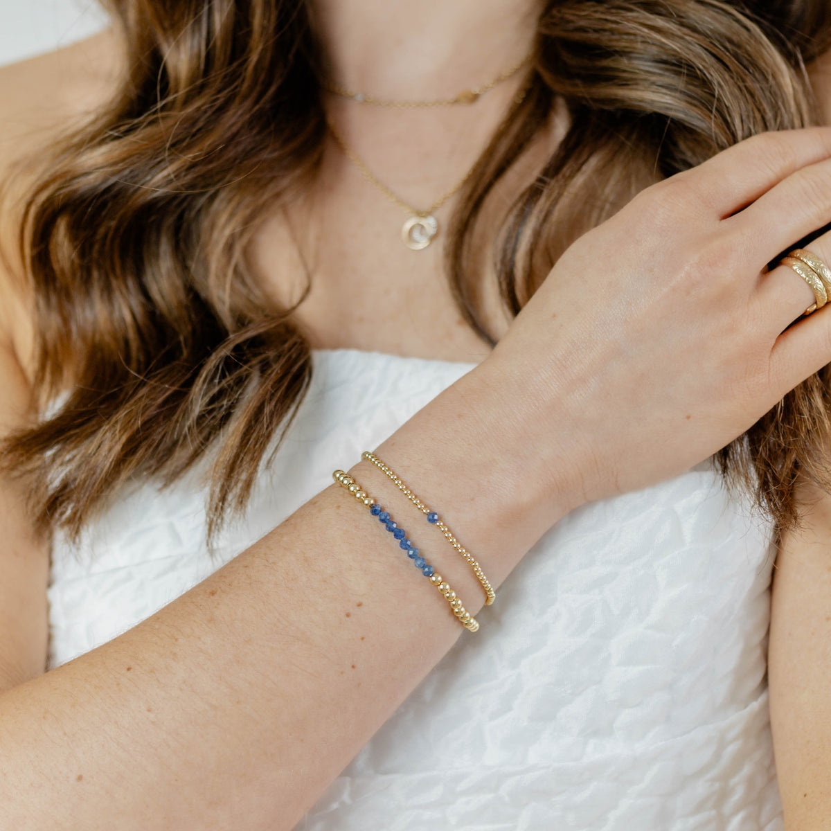 Close-up of a person wearing gold jewelry including a bracelet, necklace, and ring on a white background.